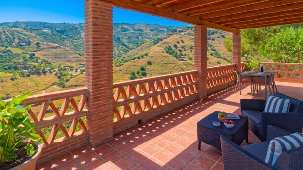 Un espace extérieur abrité, doté d’une terrasse, de colonnes en briques et offrant une vue sur des collines verdoyantes.