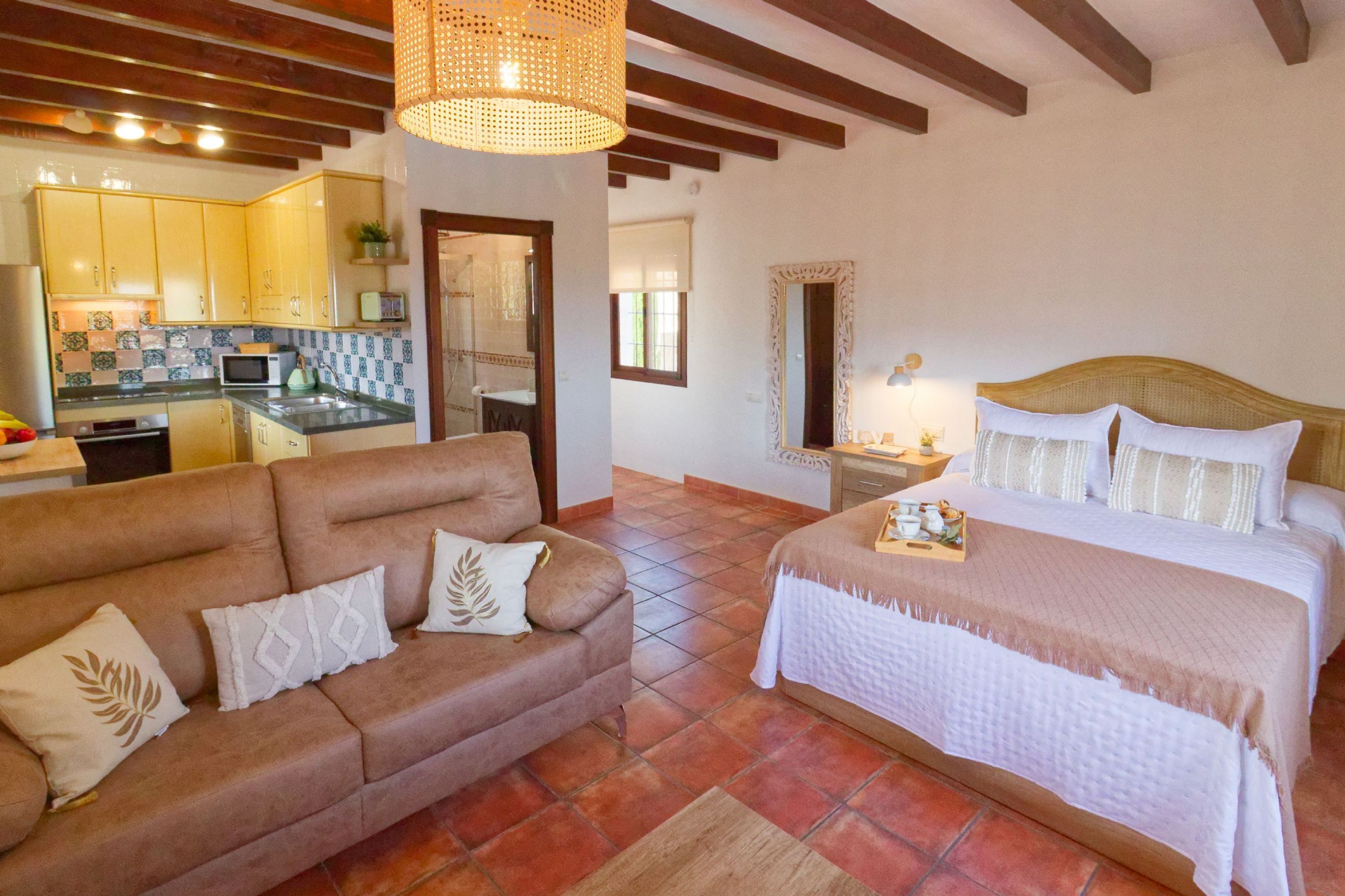 A bedroom with a bed, a sofa, and a kitchen in the background.