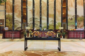 Un mostrador de recepción de diseño moderno, flanqueado por columnas verticales y un mural que representa un paisaje natural.