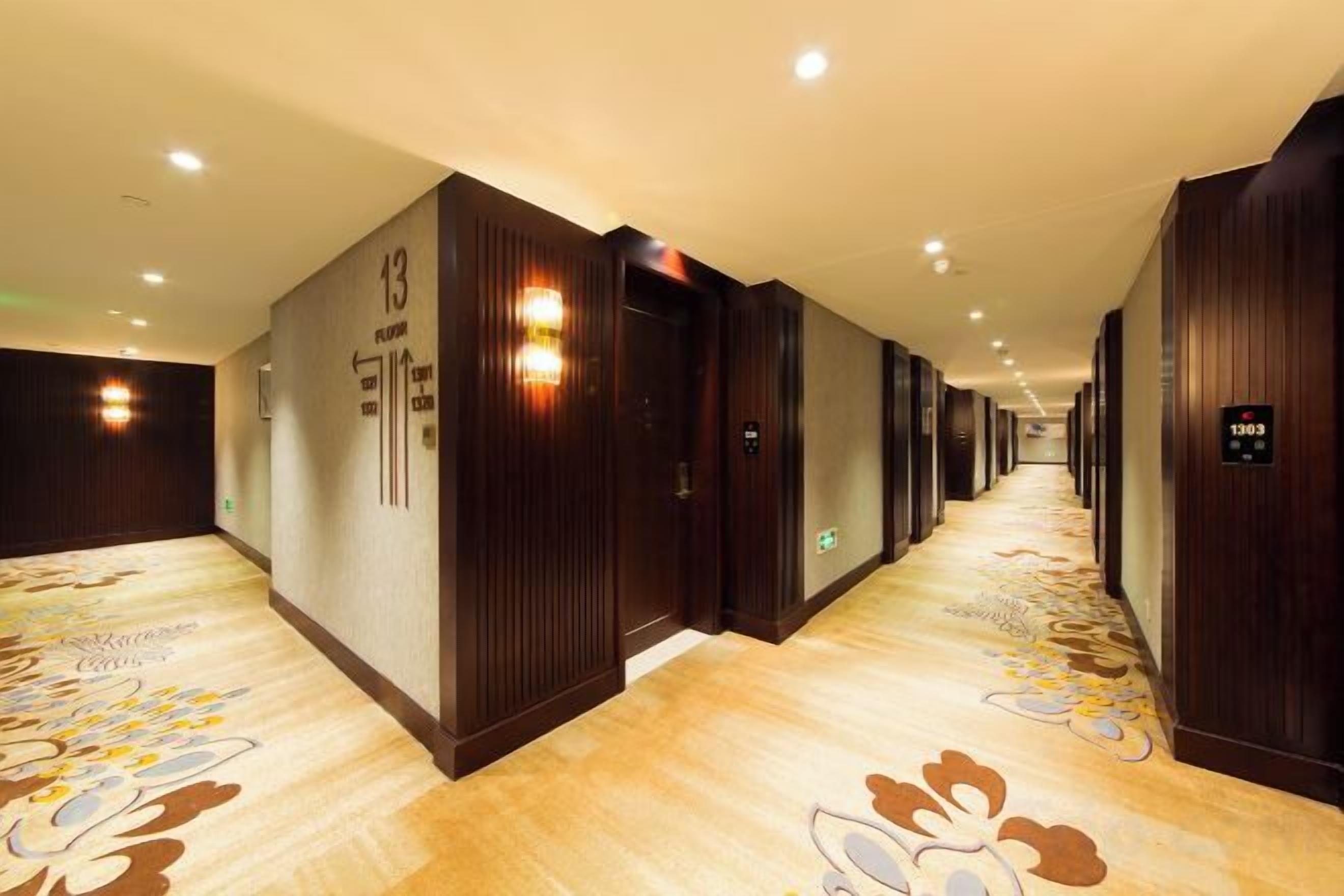 Un couloir d’hôtel aux murs en bois, aux portes numérotées et au tapis orné de motifs floraux.