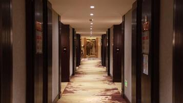 A hotel corridor with doors on both sides, a patterned carpet, and a ceiling with recessed lighting.