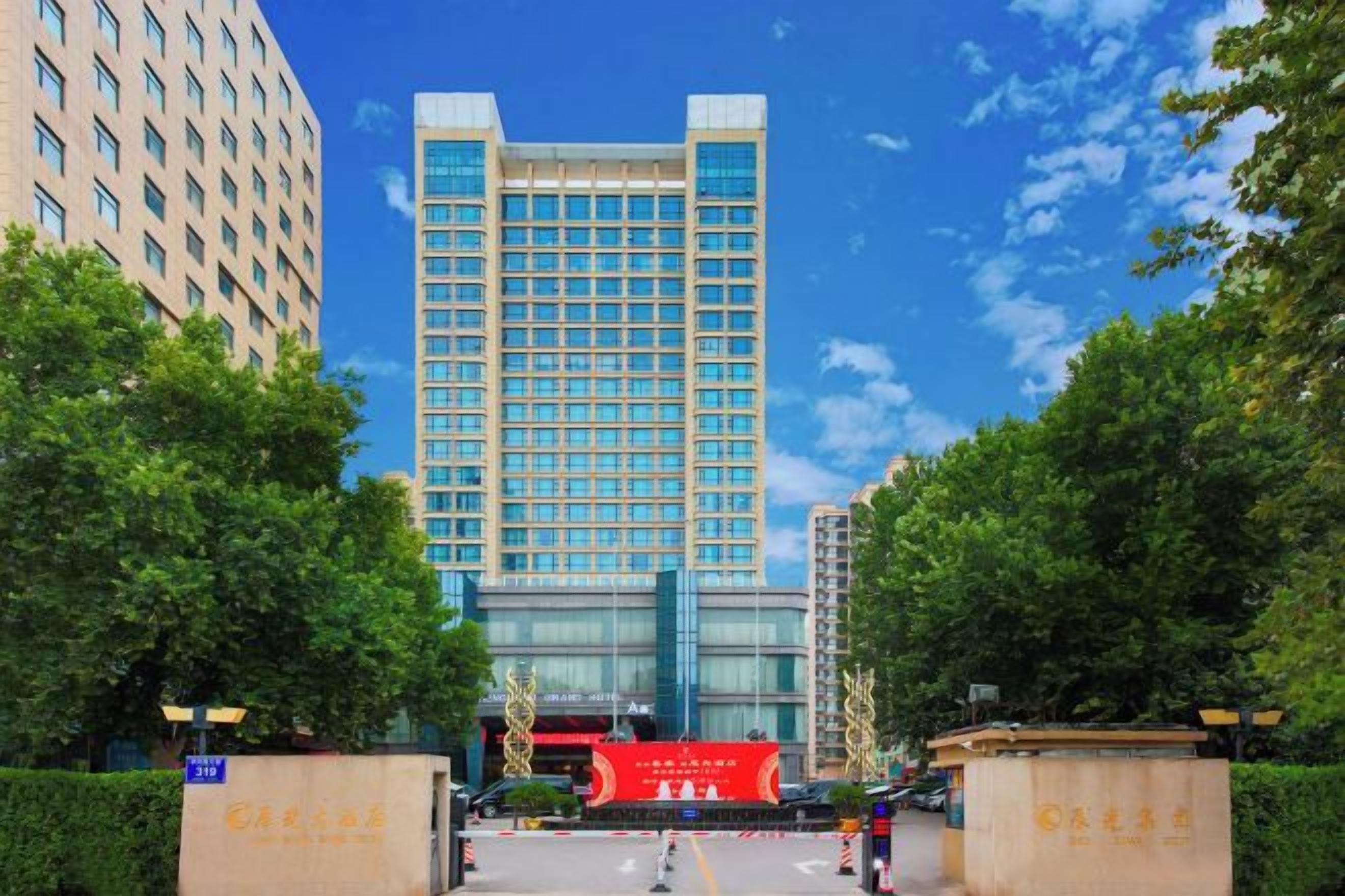 A hotel entrance with a large building in the background, a red banner, and a clear sky.