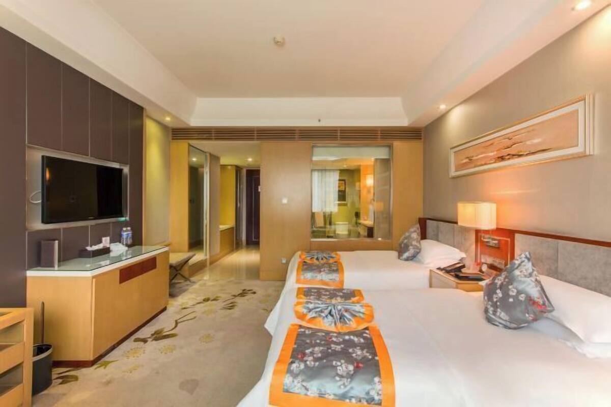 Una habitación de hotel con televisión, escritorio, cama con edredón estampado con motivos florales y espejo.