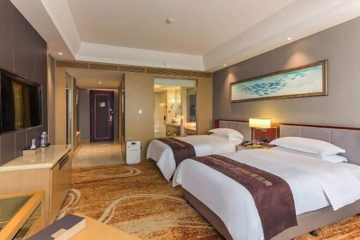 Habitación de hotel con dos camas, un escritorio, un televisor y un cuadro en la pared.