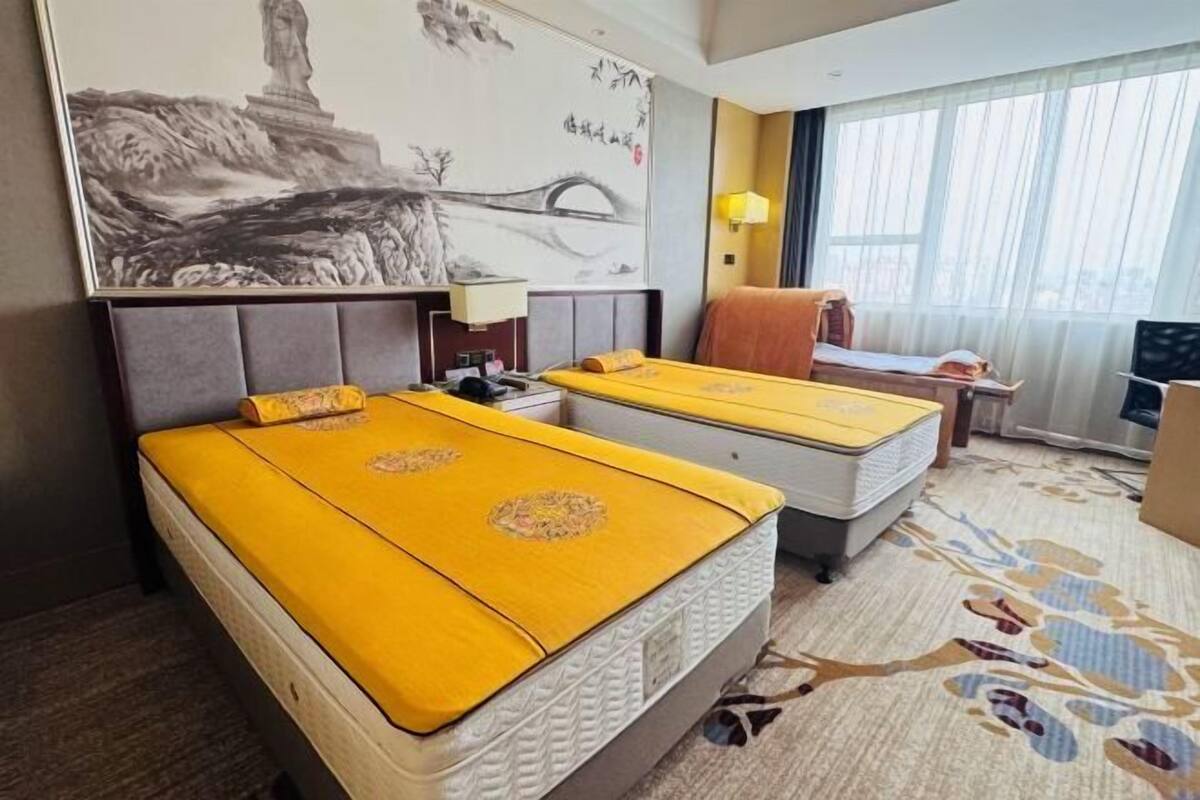 Habitación de hotel con dos camas, un ventanal grande, un cuadro en la pared y suelo alfombrado.