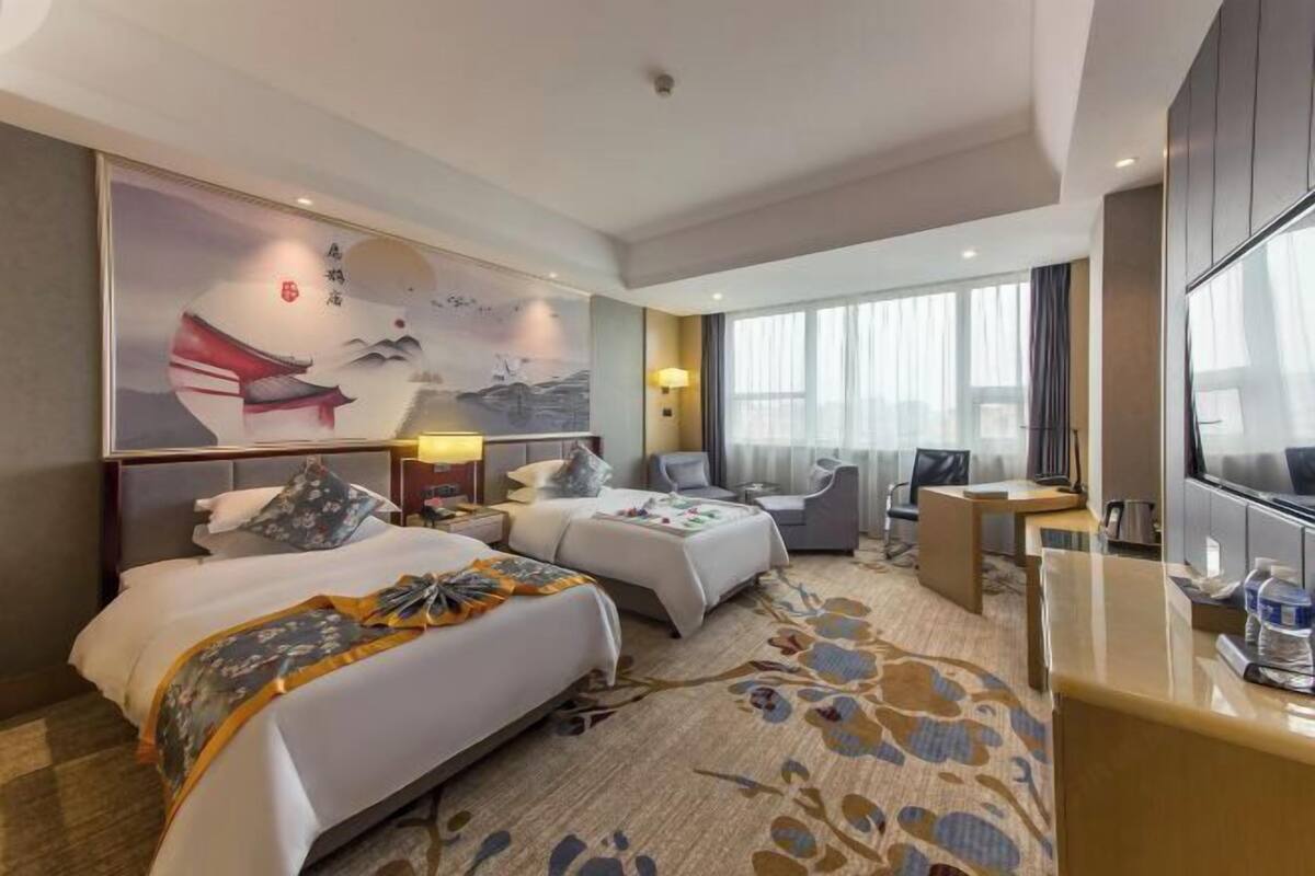 Habitación de hotel con dos camas, un escritorio, un televisor y un cuadro grande en la pared.