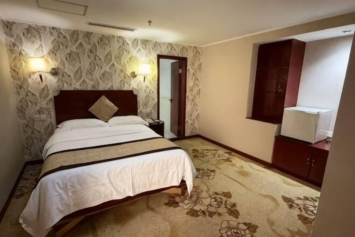 Una habitación de hotel con cama, mesita de noche, espejo, armario y suelo alfombrado.
