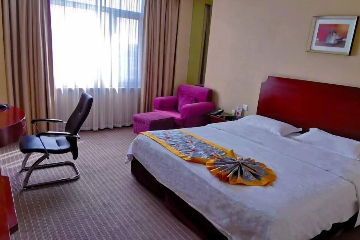 Una habitación de hotel con cama, escritorio, silla y ventana con cortinas.