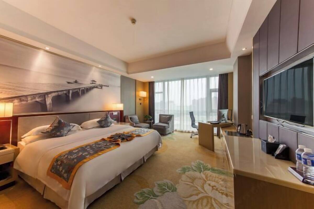 Una habitación de hotel con una cama grande, un escritorio, un televisor y un ventanal con cortinas.
