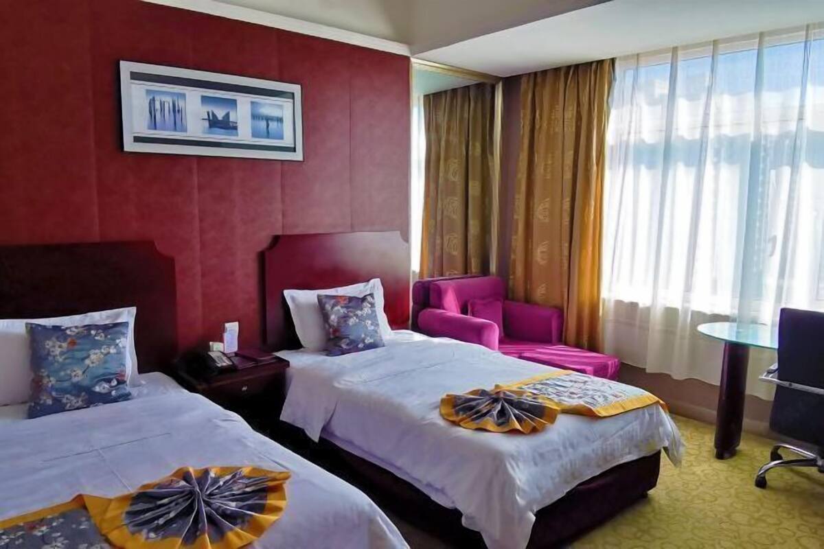 Habitación de hotel con dos camas, un escritorio, una silla y una ventana con cortinas.