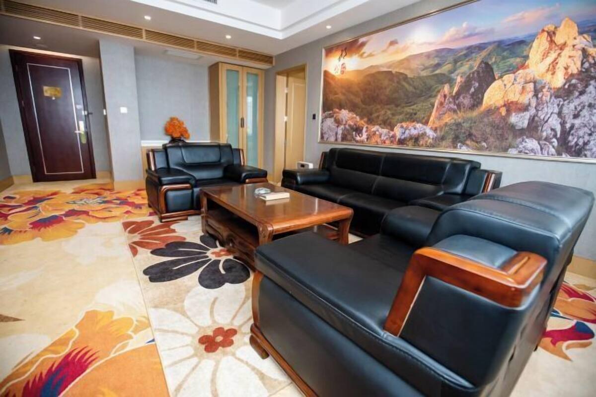 Un moderno vestíbulo de hotel con un sofá, sillas, una mesa de centro y un cuadro grande de un paisaje montañoso.