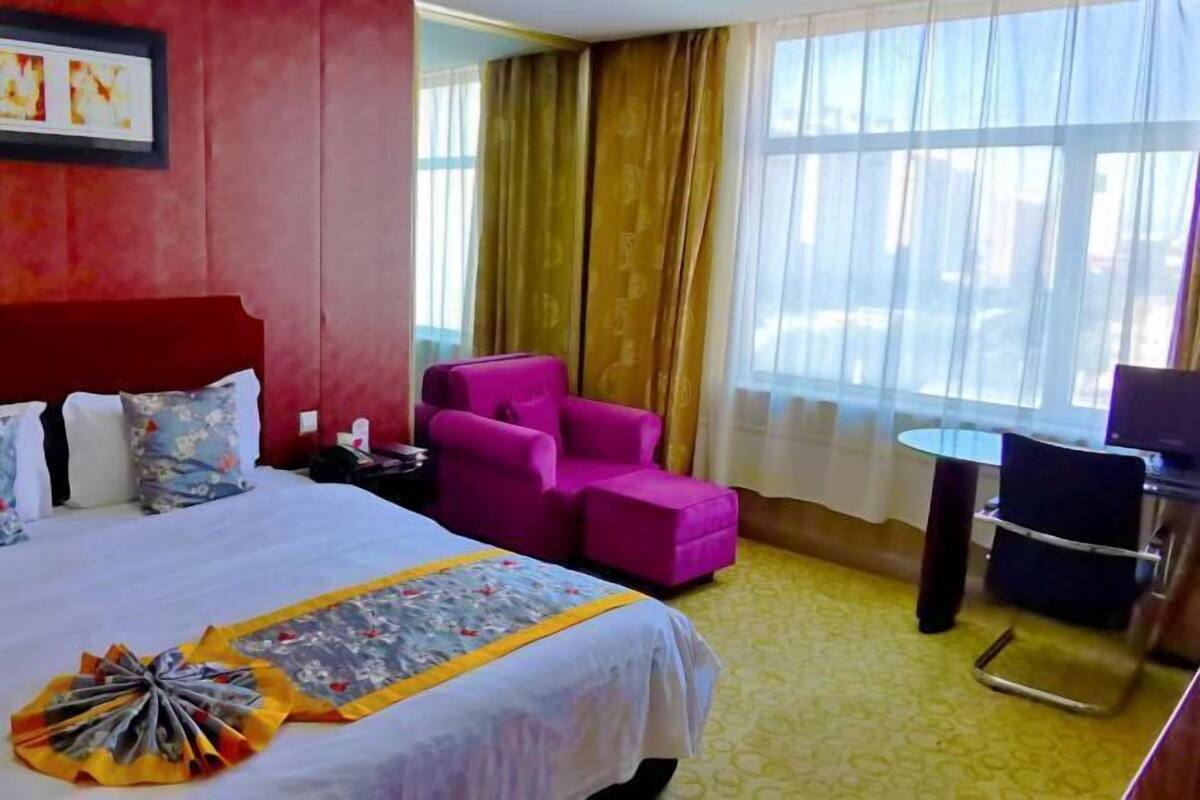Una habitación de hotel con una cama, un sillón rosa, una mesita y una silla.