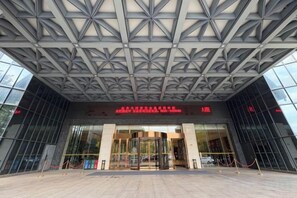 A building entrance with a geometric ceiling design, glass doors, and a red sign above the entrance. - Chenguang Hotel (Xingtai)