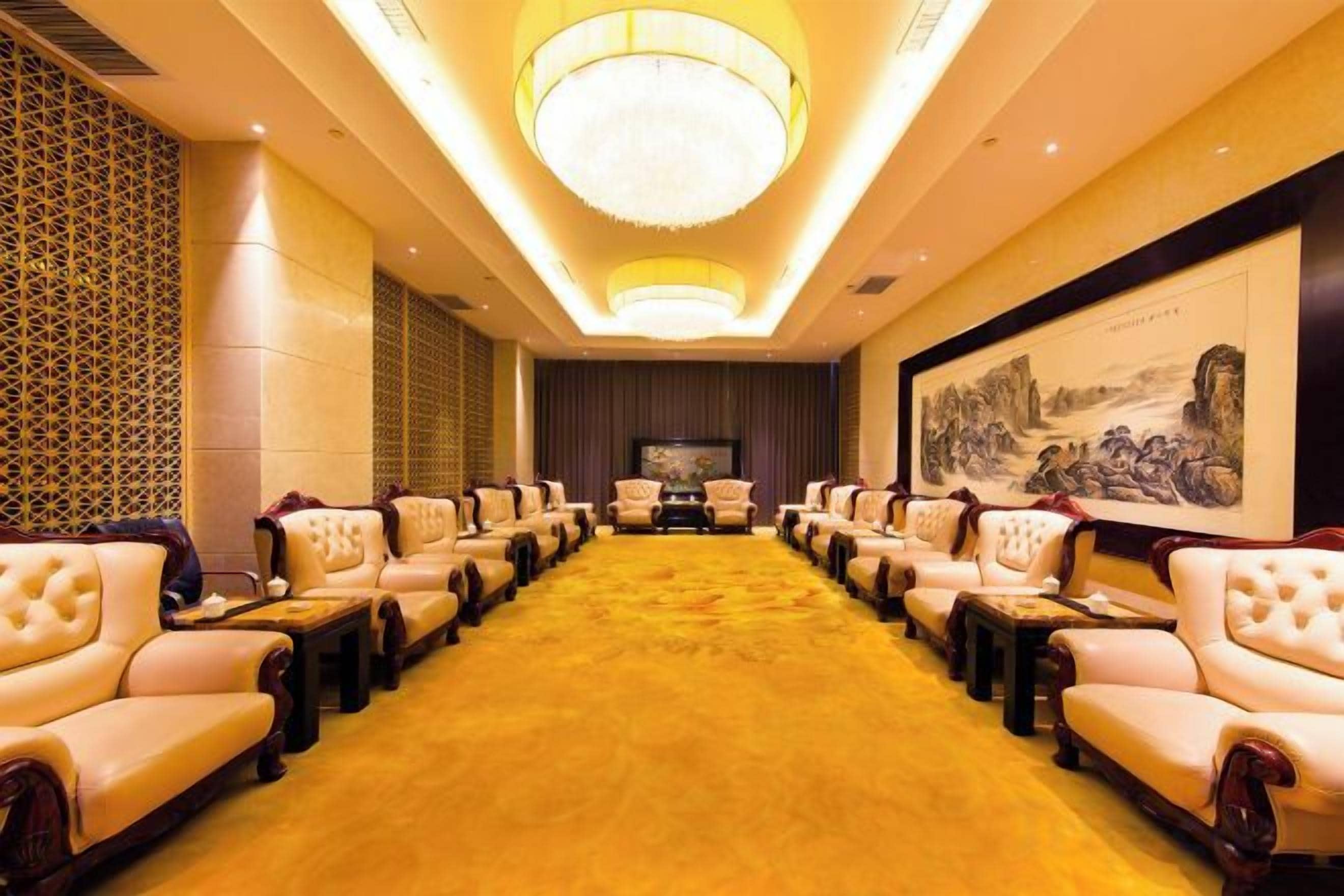 A conference room with rows of leather chairs, a large chandelier, and a framed artwork on the wall.
