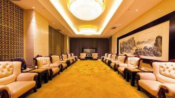 A conference room with rows of leather chairs, a large chandelier, and a framed artwork on the wall.