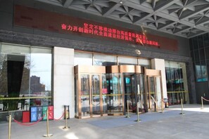 A building entrance with a glass door and a red banner above. - Chenguang Hotel (Xingtai)