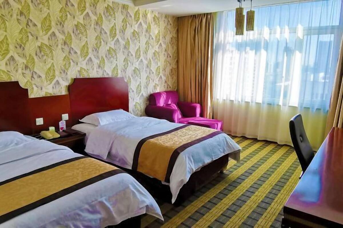 Habitación de hotel con dos camas, un escritorio, una silla y una ventana con cortinas.