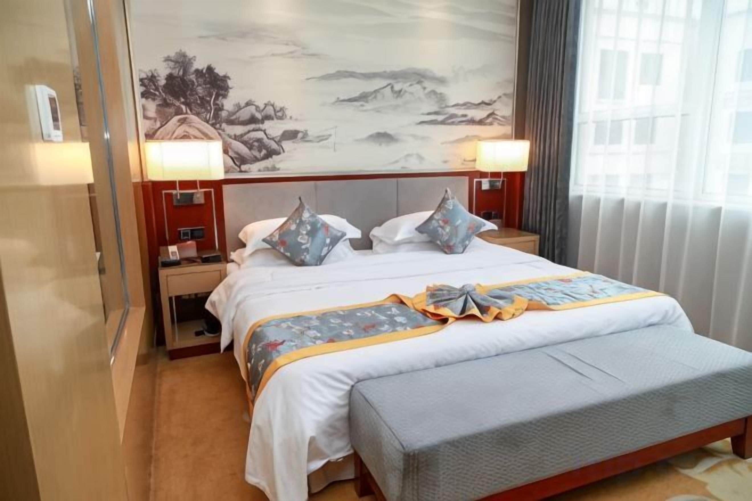 Una habitación de hotel con una cama, mesitas de noche, lámparas y un cuadro grande en la pared.