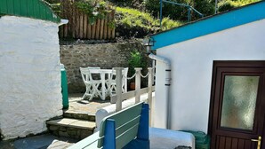 Un sendero de piedra lleva a una puerta blanca con un panel de vidrio, un banco azul y una mesa blanca con sillas.