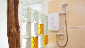 A bathroom with a shower, a glass door with yellow-tinted panels, and a wooden door frame. - The Old Cottage, Aberporth (Glanrhyd)