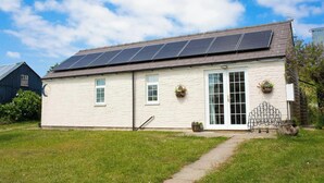 A single-story building with a stone facade, a large window, and solar panels on the roof. - The Old Cottage, Aberporth (Glanrhyd)