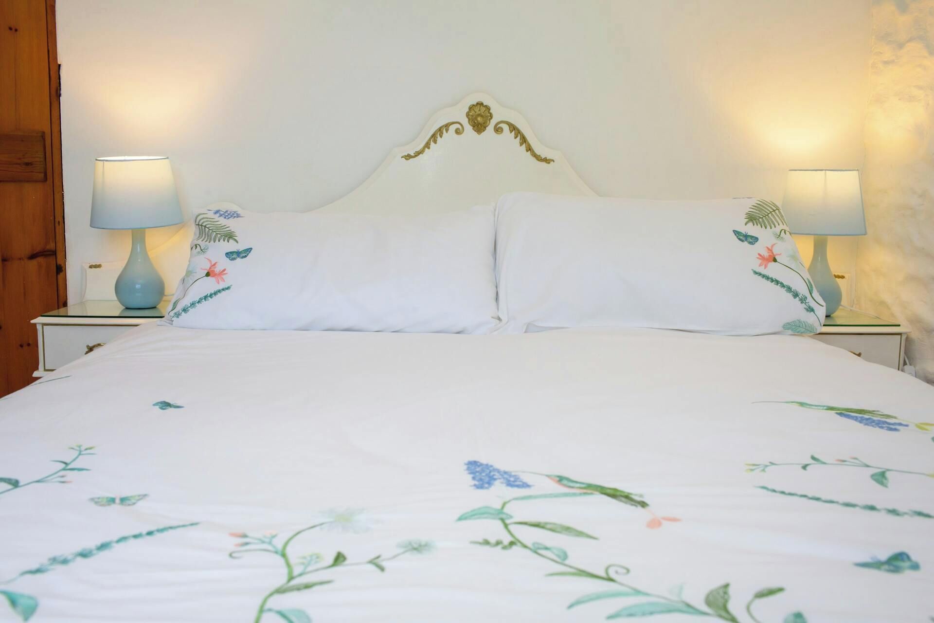 A bed with floral bedding, two bedside lamps, and a wooden nightstand.
