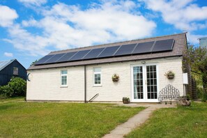 A single-story building with a sloped roof, solar panels, a white exterior, and a small garden area. - The Old Cottage, Aberporth (Glanrhyd)