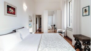 A hotel room with a bed, a small table, a chair, and a view of the hallway and another room. - Medel (Appiano Gentile)
