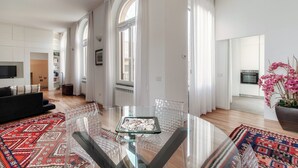 A modern living room with a glass dining table, a black sofa, and a red patterned rug. - Medel (Appiano Gentile)