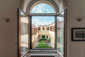 A view from a balcony with a glass door leading to a courtyard with buildings and greenery. - Medel (Appiano Gentile)