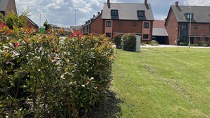 A residential area with modern brick houses, a well-maintained lawn, and a clear sky. - Honeybee Haven Retreat - 3 Bed House (Ashford)