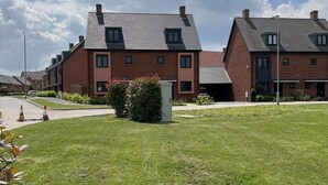 A residential area with modern brick houses, a well-maintained lawn, and a clear sky. - Honeybee Haven Retreat - 3 Bed House (Ashford)