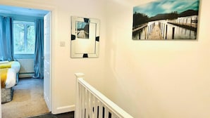 Un couloir avec un escalier, un lit avec des rideaux bleus et un tableau encadré accroché au mur.