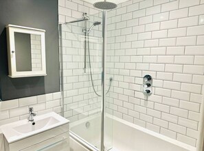 Ett modernt badrum med en duschavdelning med glasväggar, vita kakelplattor i tunnelbanemodell, en vit tvättställ och en spegel.