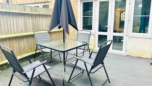 Une terrasse avec une table en verre et quatre chaises, un parasol et une clôture en bois.