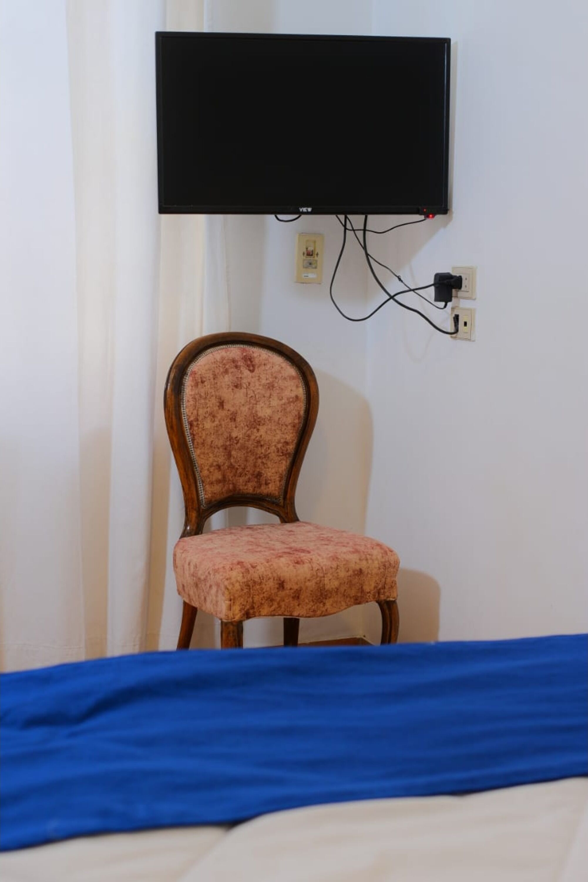 A room with a bed, a chair, and a flat-screen TV mounted on the wall.