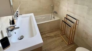 Une salle de bain avec un lavabo blanc, une baignoire et une fenêtre.