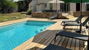 Une piscine entourée d’une terrasse en bois, de chaises longues et de parasols.
