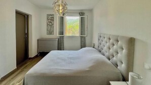 Une chambre à coucher avec un grand lit, un lustre, une fenêtre donnant sur un beau paysage et une commode.