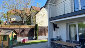 Une maison moderne dotée d’un patio, d’une petite maison de jeux et d’un coin repas avec du mobilier d’extérieur.