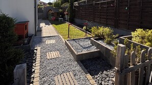 Un étroit sentier mène à une maison entourée d’une clôture en bois et dotée d’un petit jardin.