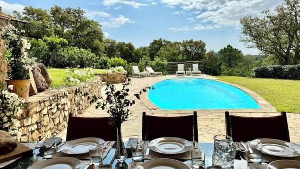 Spiseområde med udsigt til swimmingpool og grønne omgivelser.