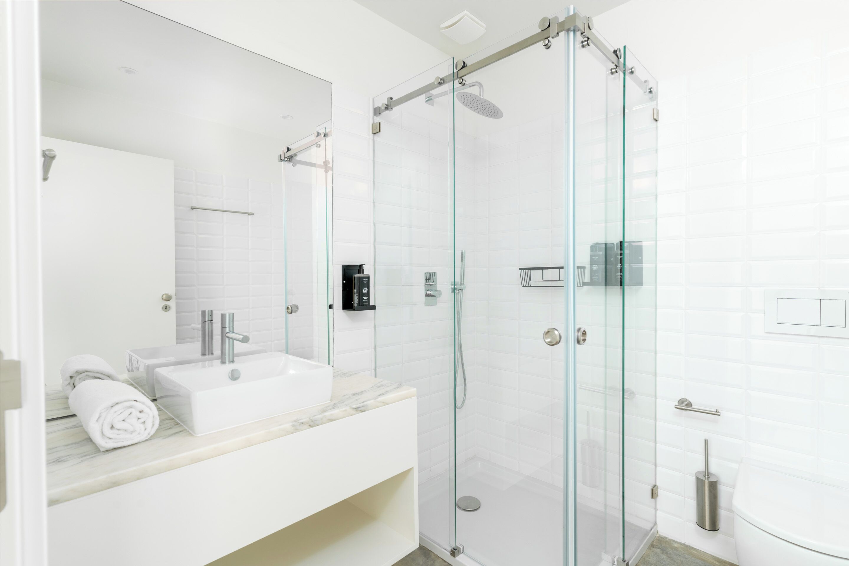 A modern bathroom with a glass-enclosed shower, a white sink, and a marble countertop.