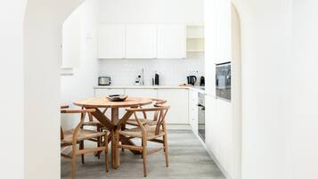 A modern kitchen with white cabinetry, a round wooden table, and a built-in oven.