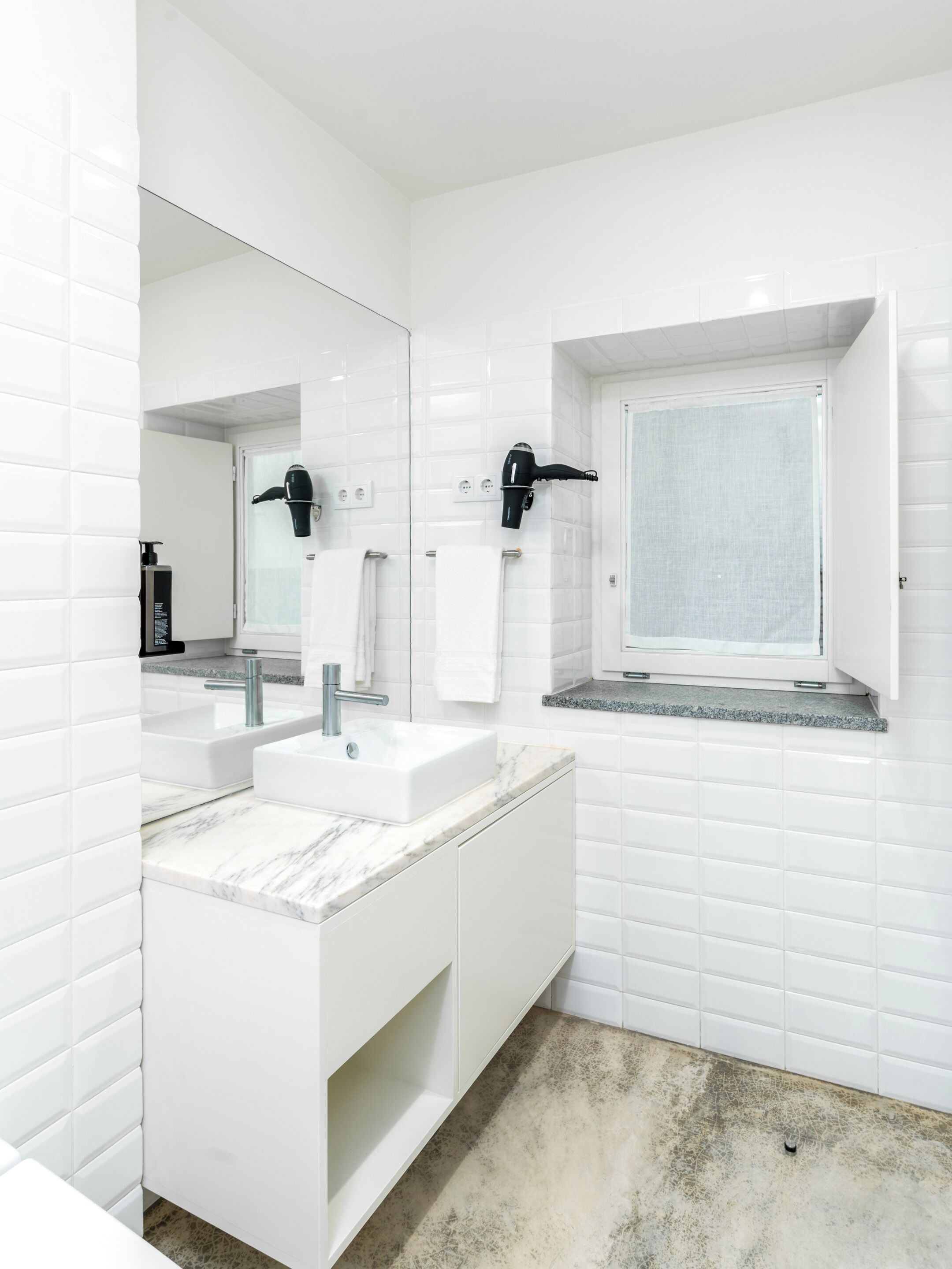 A modern bathroom with white tiled walls, a marble countertop sink, and a large mirror.