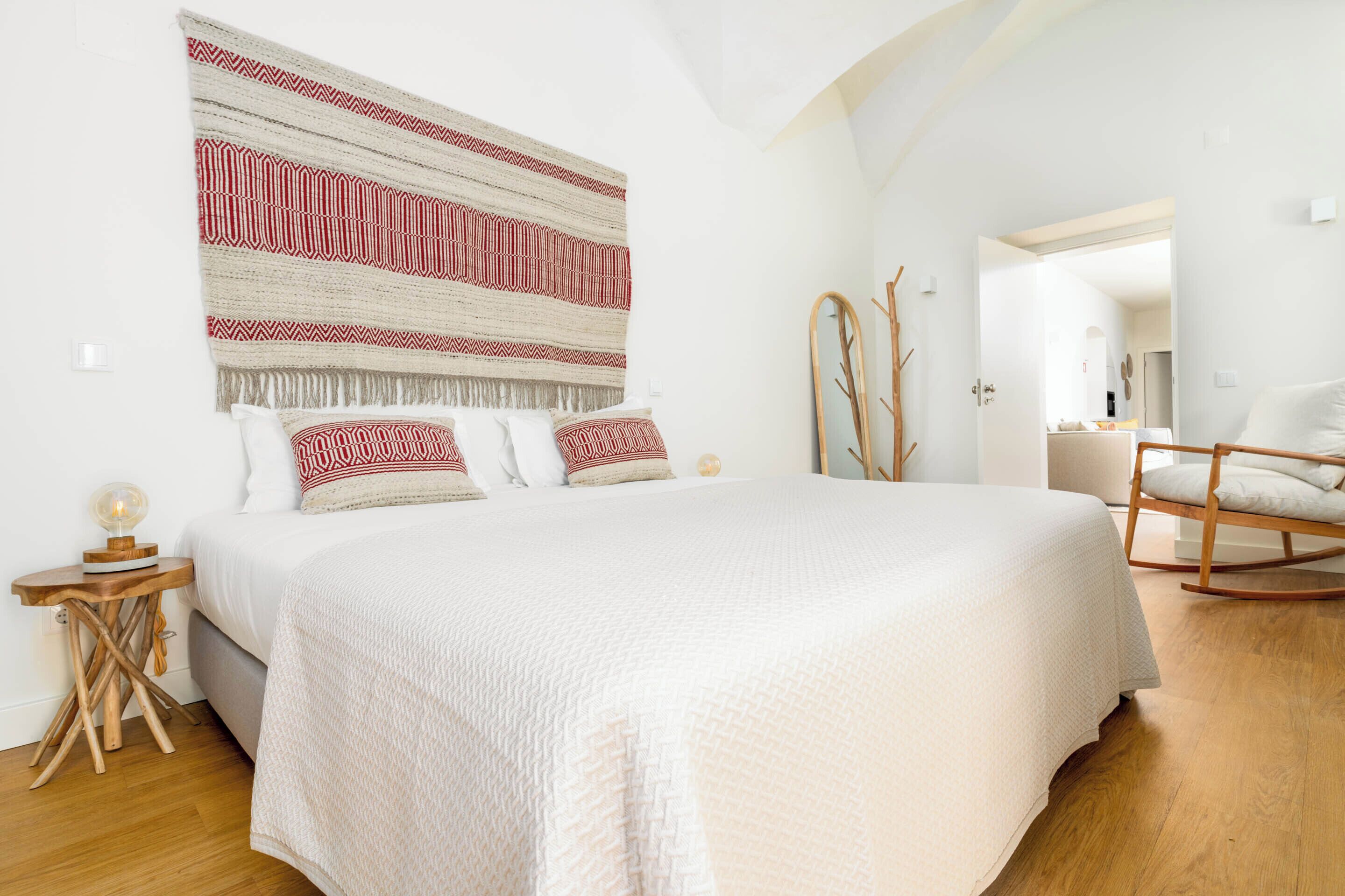 Un dormitorio con una cama grande, una mesita de noche de madera, un espejo y una mecedora.