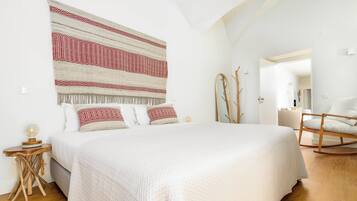 Un dormitorio con una cama grande, una mesita de noche de madera, un espejo y una mecedora.