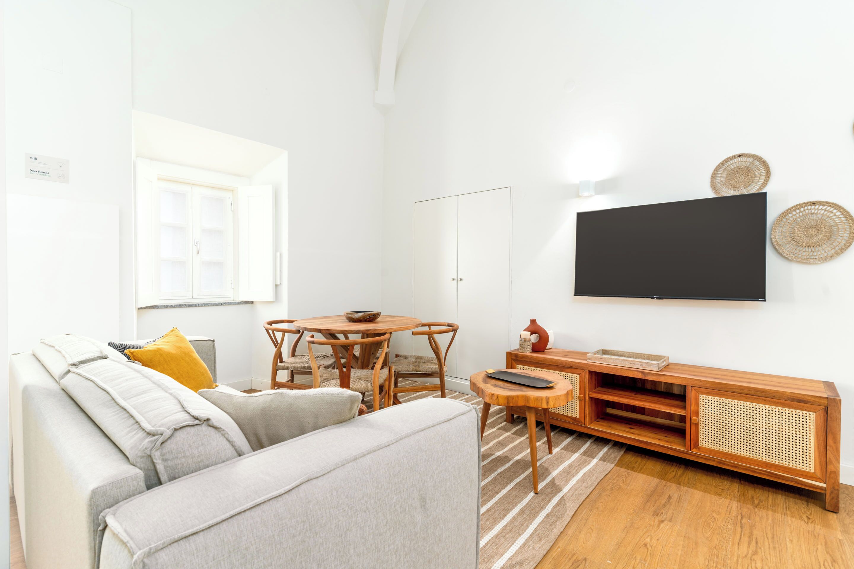Un salon comprenant un canapé, une table à manger avec des chaises, un téléviseur fixé au mur et un meuble de rangement en bois.