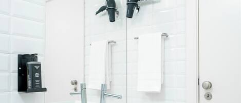 A modern bathroom with white tiled walls, a white vanity with a marble countertop, a large mirror, a towel rack, and a door with a keyhole.