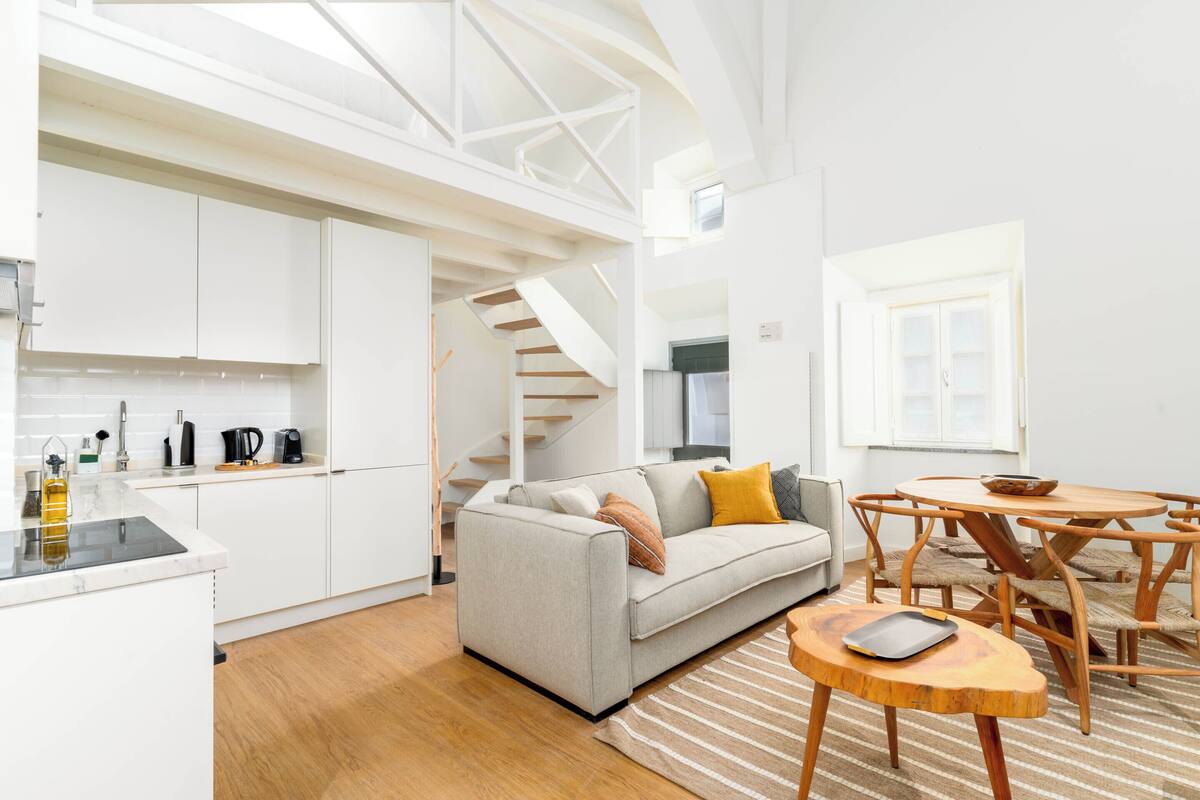 A modern interior with a kitchen, a sofa, a dining table, and a staircase.
